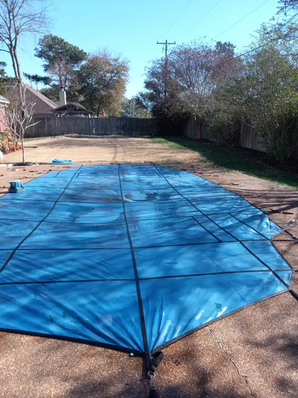 Long freeform pool under a blue mesh safety cover